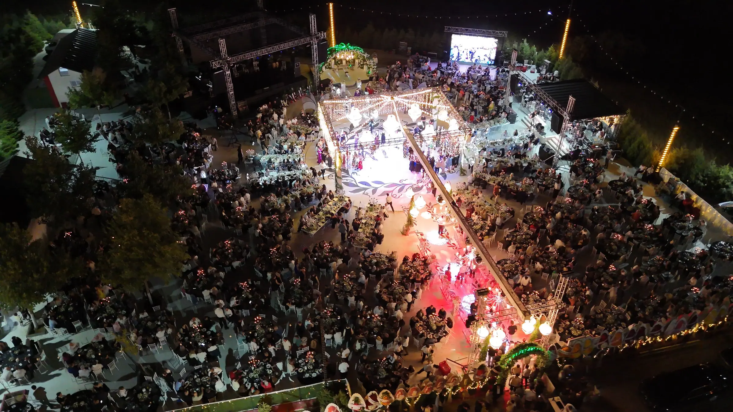 Gece ışıklandırılmış sünnet töreni; ortadaki podyumda dans eden kalabalık ve renkli sahne ışıkları